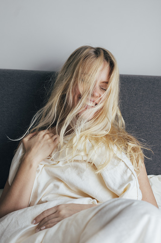 快乐的早晨:漂亮的金发女人长凌乱的头发坐在床上笑图片素材