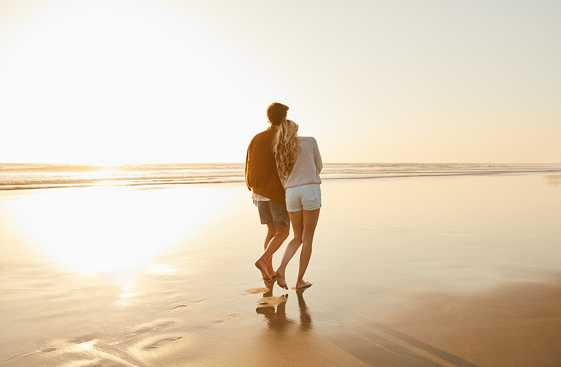 傍晚时分，一对年轻夫妇在海滩上散步图片下载