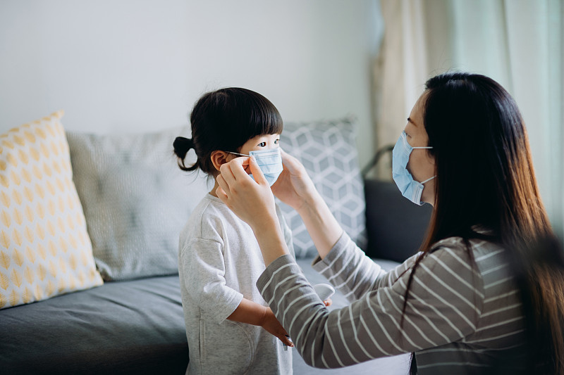 年轻的亚洲母亲在出发前为小女儿戴上外科口罩，以防止感冒、流感和病毒的传播图片下载