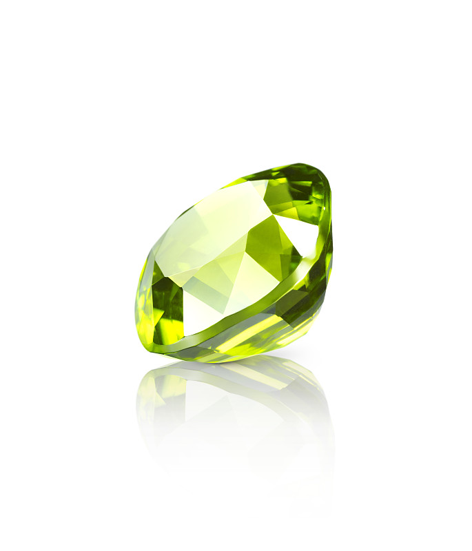 闪光的浅绿色橄榄石宝石躺在一个白色的表面上的一个下降的阴影和反射的近对角线视图图片素材