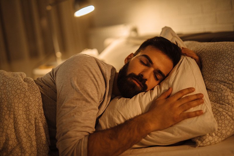 年轻人抱着柔软的白色枕头睡在床上图片素材