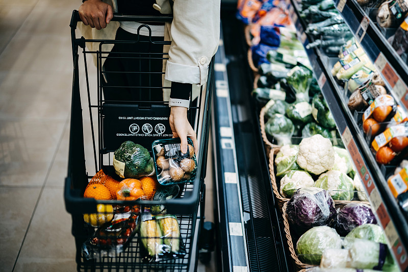 近距离的女人的手在超市购买新鲜的食品杂货，并把各种有机蔬菜在购物车图片下载