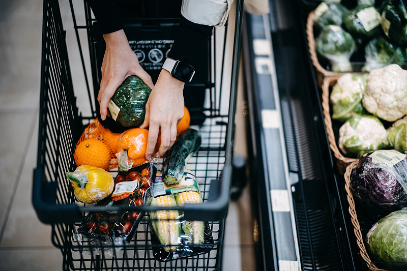 近距离的女人的手在超市购买新鲜的食品杂货，并把各种有机蔬菜在购物车图片下载
