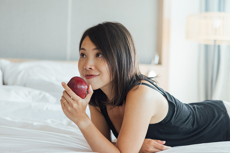 微笑的年轻女子在床上拿着一个苹果的肖像图片下载
