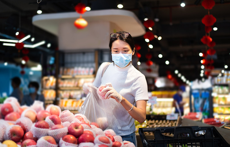 在市场上买水果的亚洲妇女戴着面具和手套图片下载