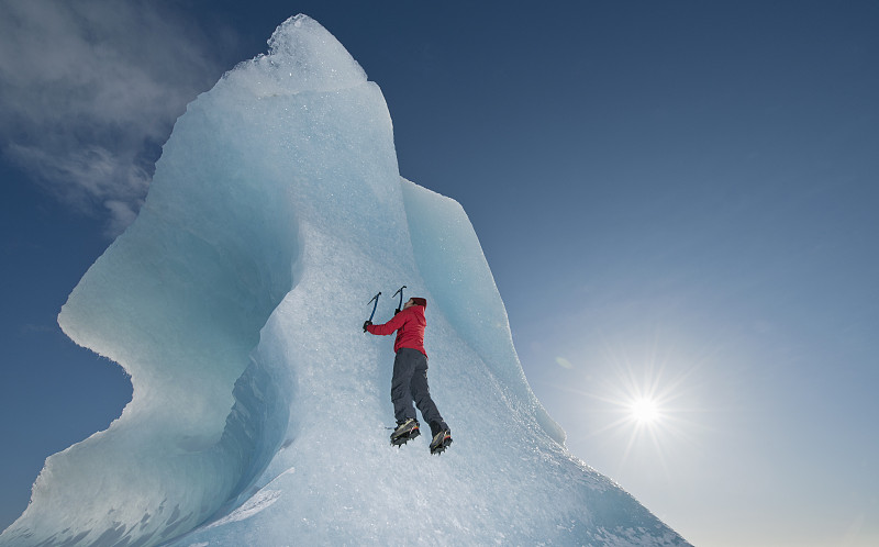女子爬上Fjallsjoull冰川泻湖上的冰山图片素材