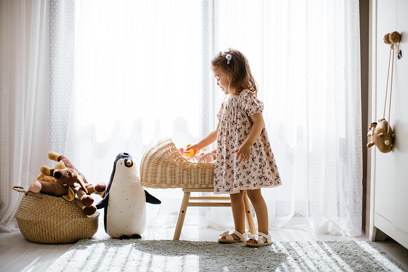 可爱的小女孩在婴儿床里喂她的玩具娃娃，在有大窗户的阳光卧室里玩图片下载
