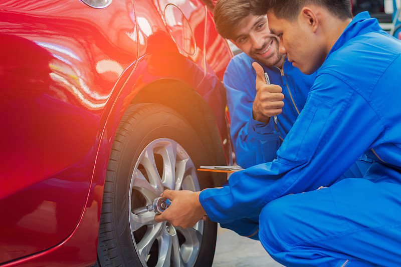 微笑的机械师向修理汽车轮子的同事竖起大拇指图片素材
