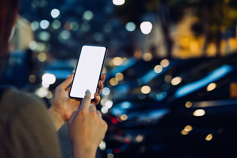 这张照片拍摄的是一位女士在城市的停车场用智能手机走到她的车旁时的手摄影图片