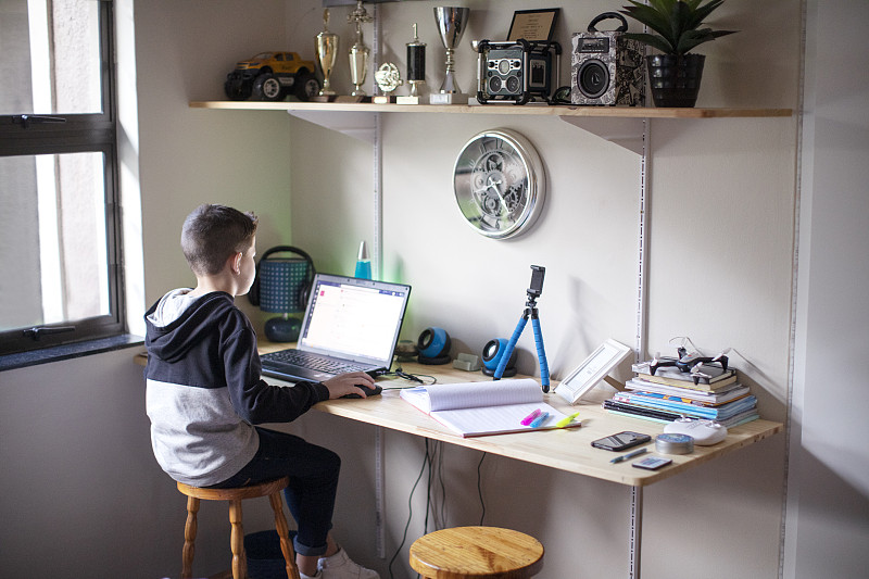一个九岁的男孩在家里用笔记本电脑做作业。图片下载