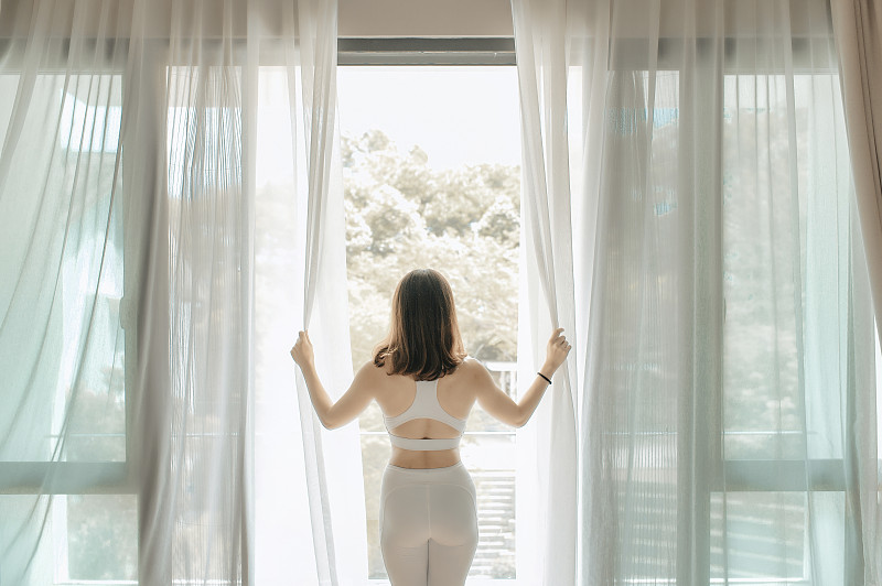 早上，一位亚洲的中国美女拉开窗帘，走到阳台上，准备练瑜伽图片素材