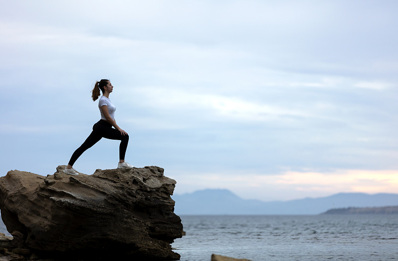 一个女人在海滩的岩石上做瑜伽图片素材