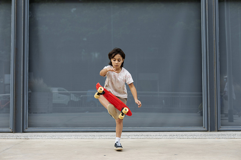 靠墙站在人行道上练习滑板特技的男孩图片下载