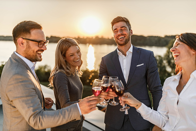 快乐的企业家们在阳台上用红酒敬酒。图片下载