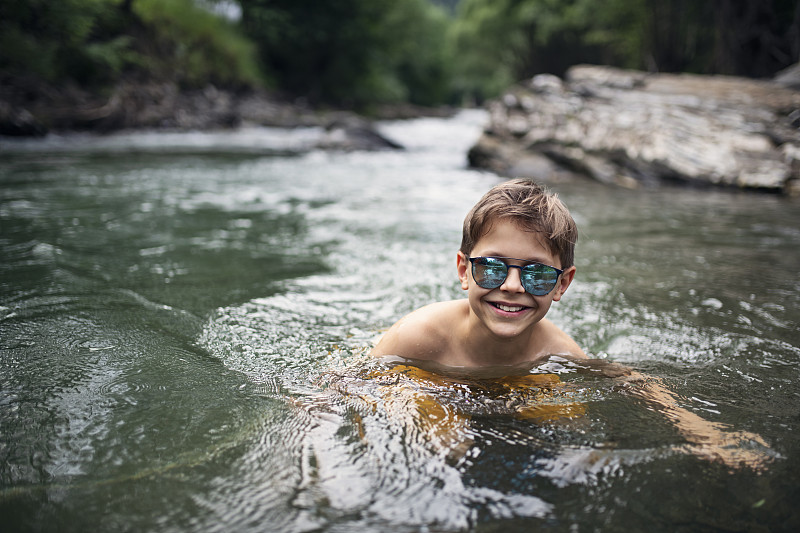 小男孩喜欢在冰冷的山间河里游泳图片素材