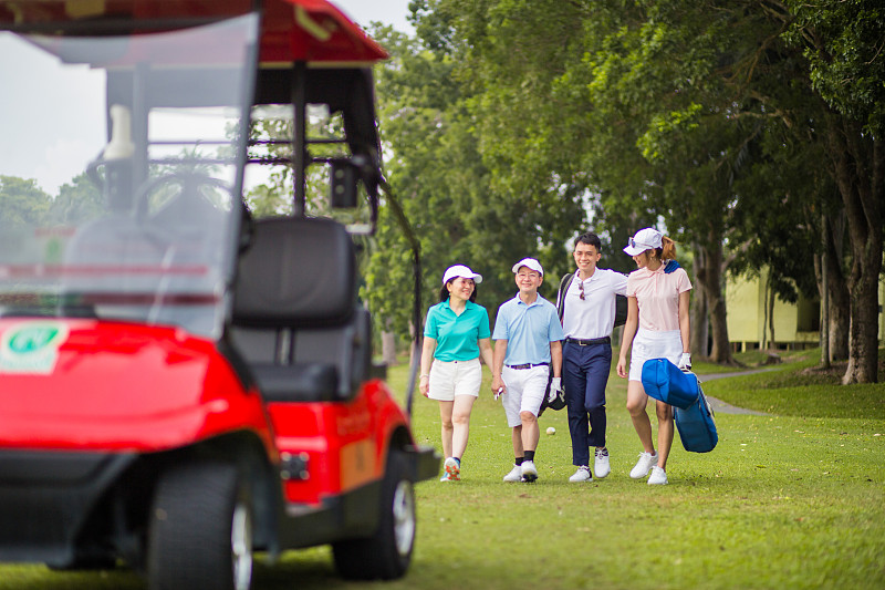 一个亚洲华人家庭微笑着在高尔夫球场享受他们的周末活动。他们正走向高尔夫球车。图片下载