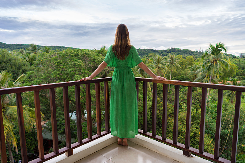 热带国家阳台上穿着绿色衣服的年轻漂亮女人图片下载