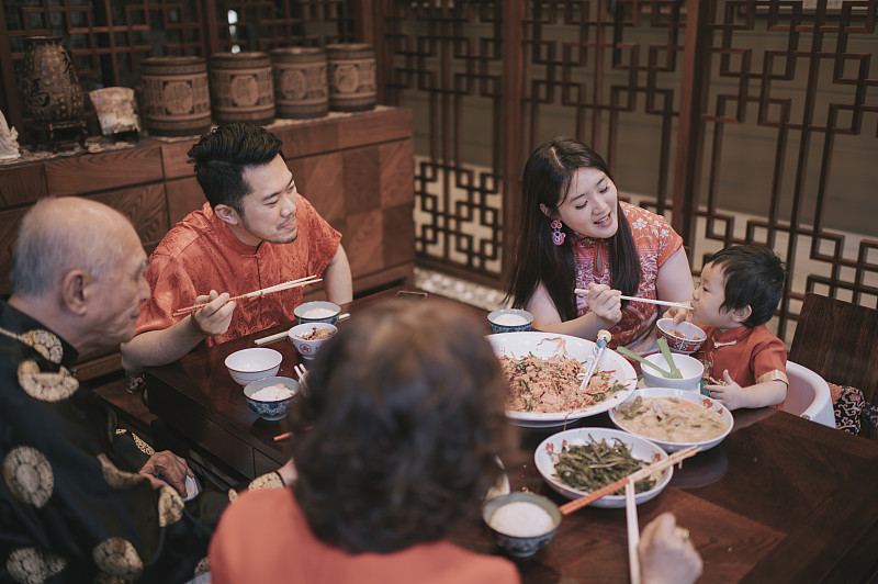 亚洲华人母亲喂她的儿子在家庭春节团圆饭与传统菜肴生鱼刘生图片素材