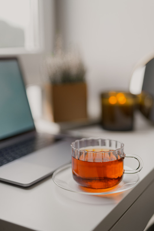 舒适的家庭氛围笔记本电脑，一杯茶和蜡烛放在靠近窗户的桌子上图片下载