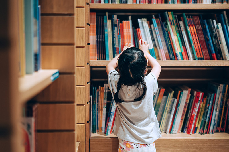 亚洲小女孩在图书馆的书架上挑选书籍图片下载