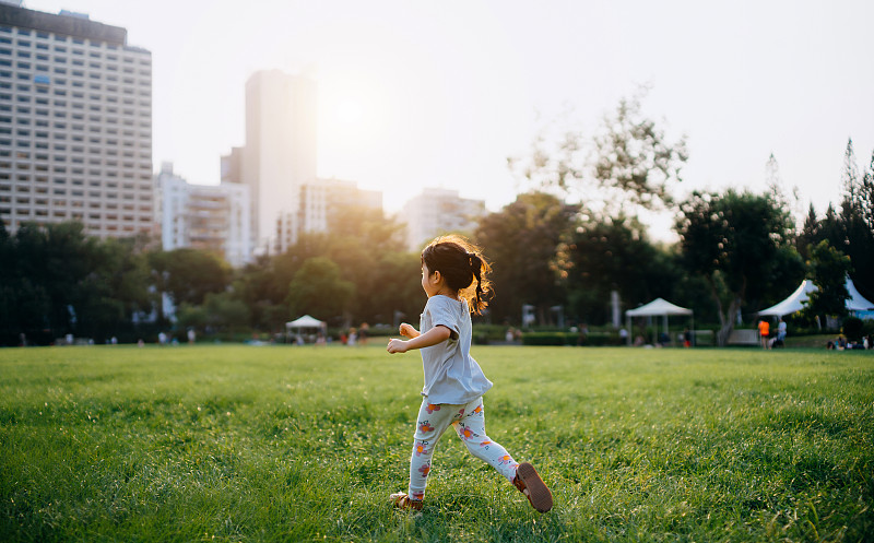 快乐的亚洲小女孩在户外玩得很开心，在朝着城市的草坪上跑来跑去，在城市公园的夕阳下享受夏日。家庭生活方式。逍遥自在概念图片下载
