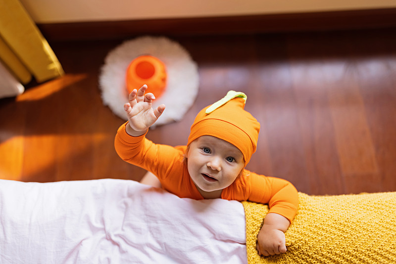 可爱的白种人婴儿，一岁的小女孩，穿着橙色的服装，家里有南瓜脸。万圣节快乐概念图片下载