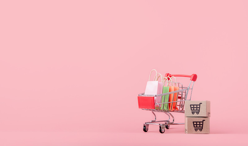 购物概念:粉红色背景的红色购物车里的纸箱或纸盒和购物袋。网上购物的消费者可以在家购物和送货上门。与复制空间图片下载