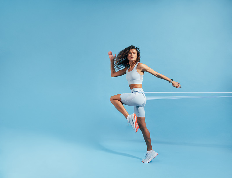 女性锻炼与阻力带在蓝色的背景。用橡皮筋锻炼的白人女运动员。图片下载