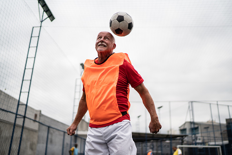年长的男子跳着用他的头在足球场击球图片下载