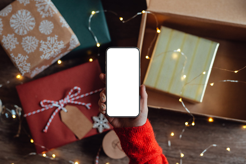 女性手持智能手机，背景中有各种各样的圣诞礼物图片下载