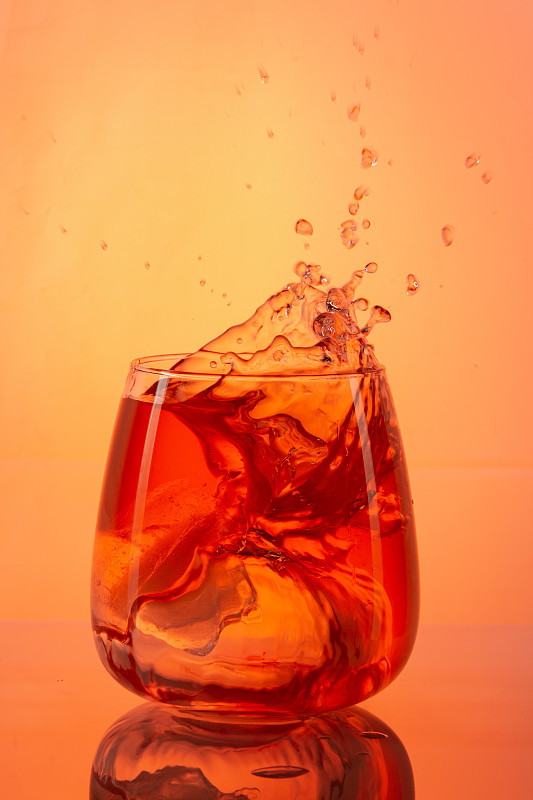 垂直拍摄的橙色鸡尾酒溅在橙色的背景图片下载