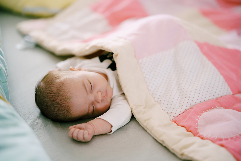 宝宝睡在铺着粉红色拼布被子的床上图片下载