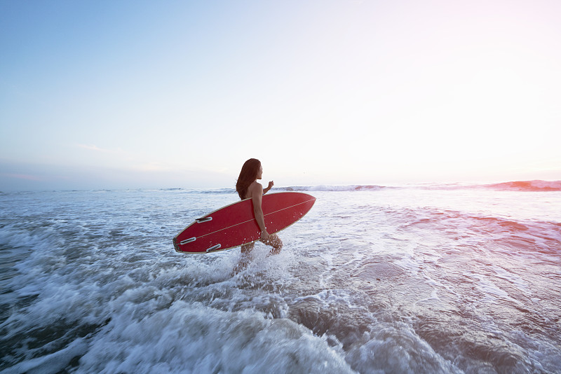 一个年轻女人拿着冲浪板走进了海浪图片下载