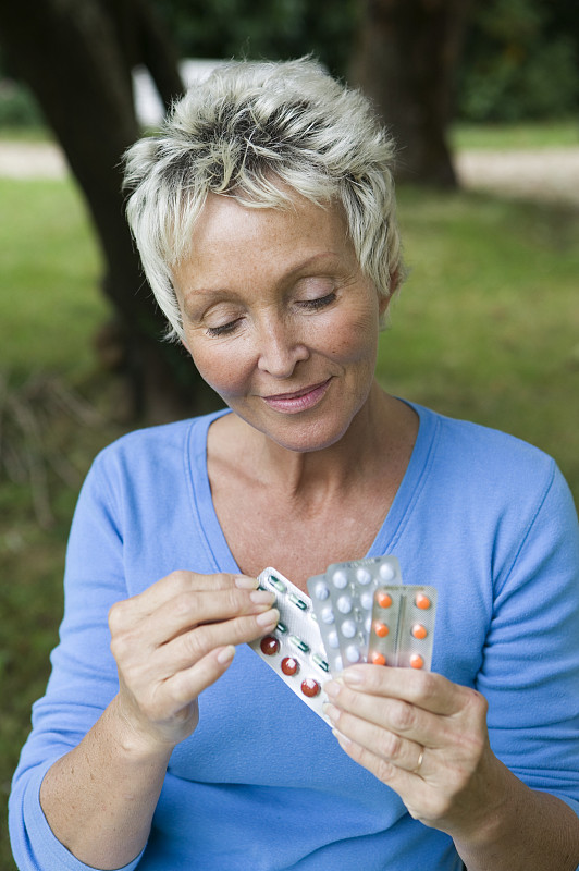 一个成熟的女人拿着各种包装的药丸，在公园里图片下载