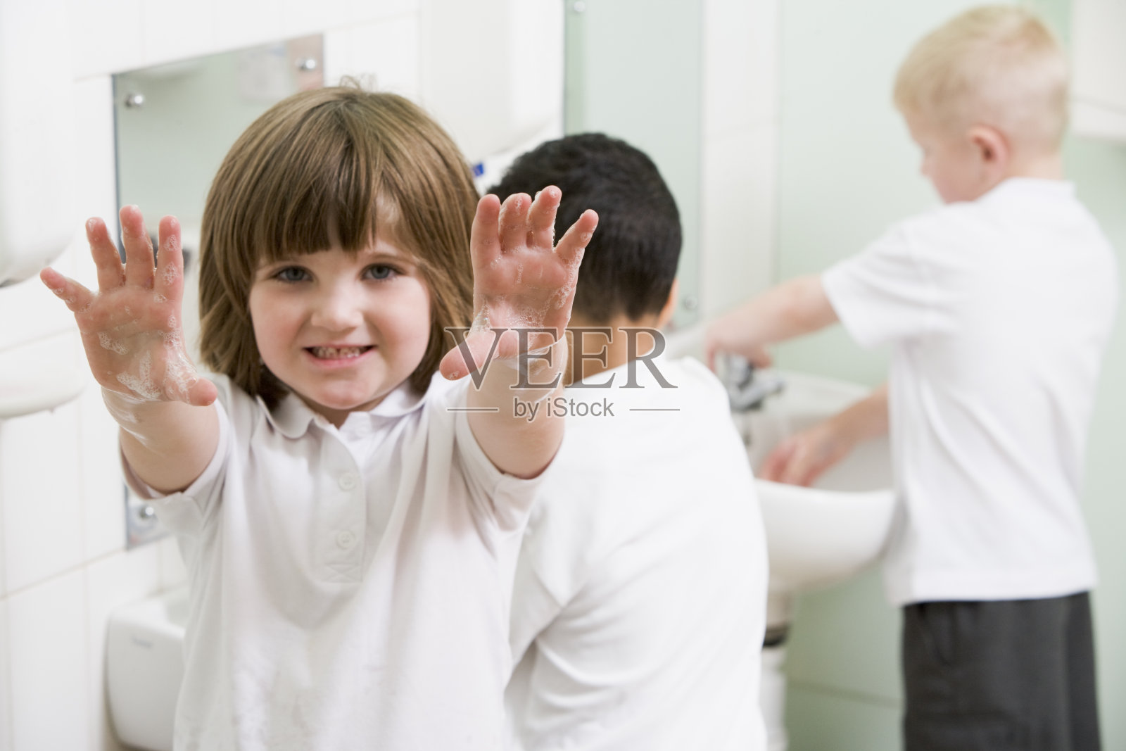 小女孩在一所小学的浴室里展示她涂了肥皂的手照片摄影图片