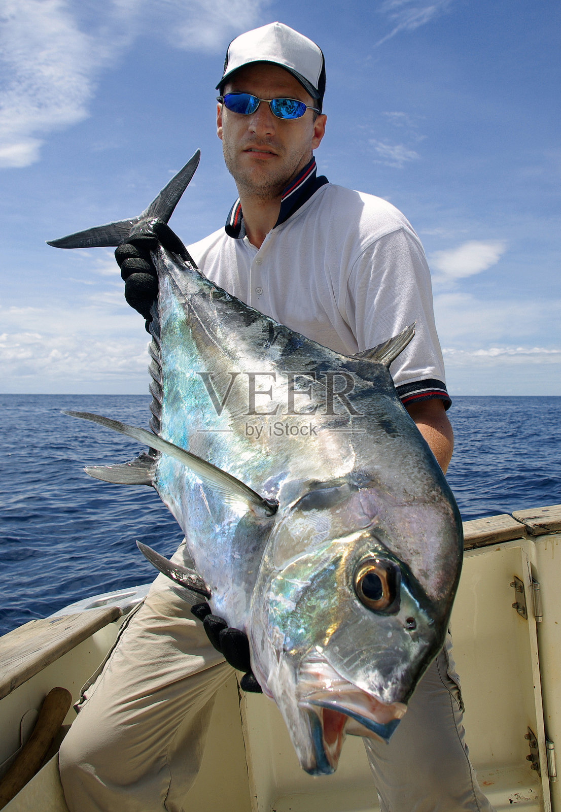 一个人在船上拿着一条特雷维利杰克鱼照片摄影图片