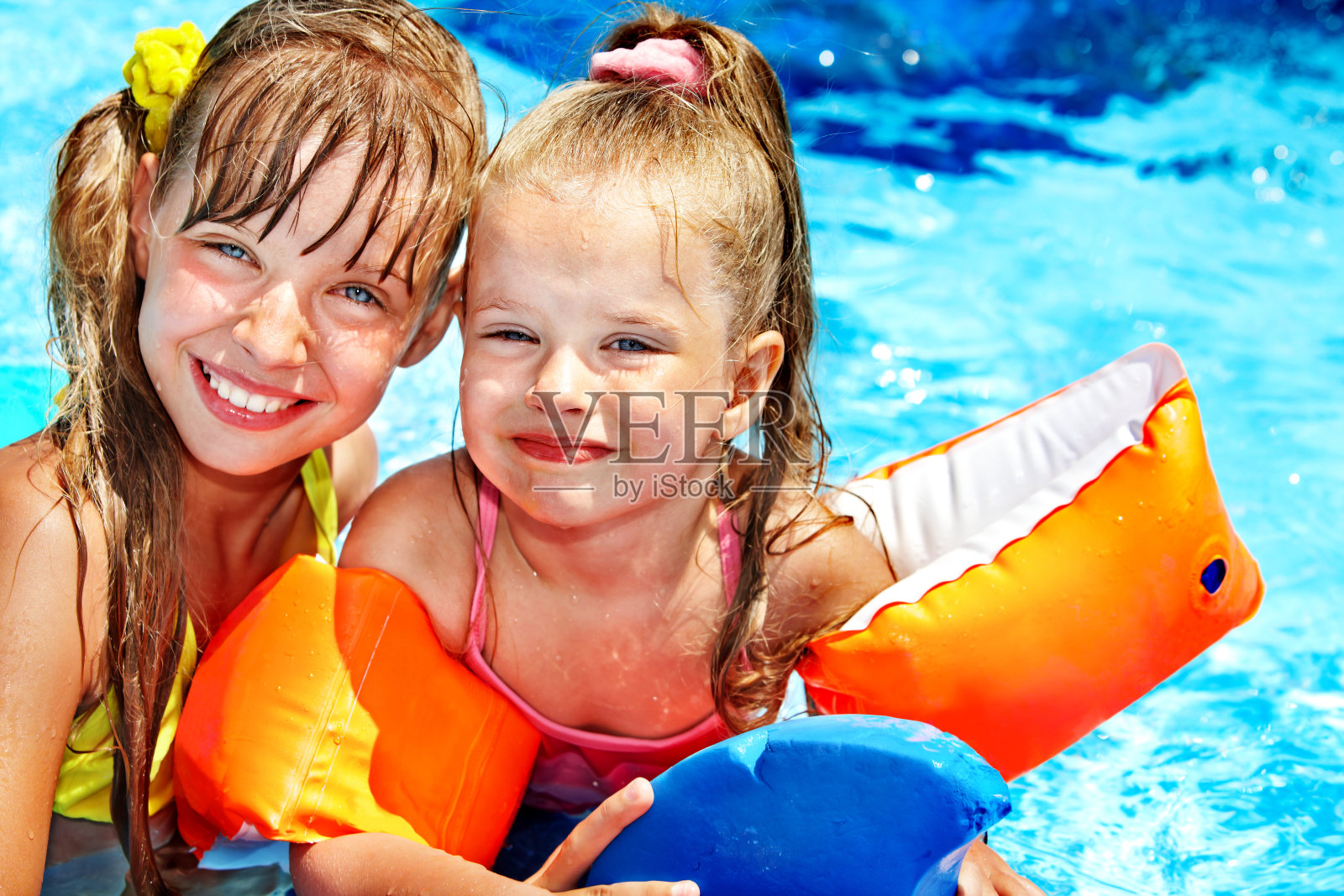两个小女孩，一个戴着臂章，在游泳池里照片摄影图片