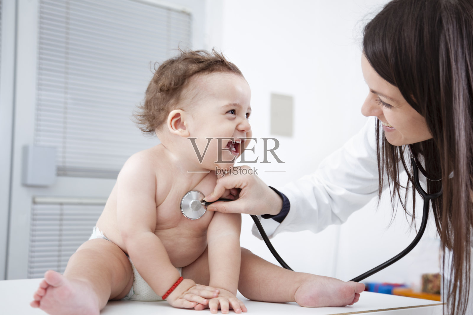女医生听着微笑的婴儿的心跳照片摄影图片