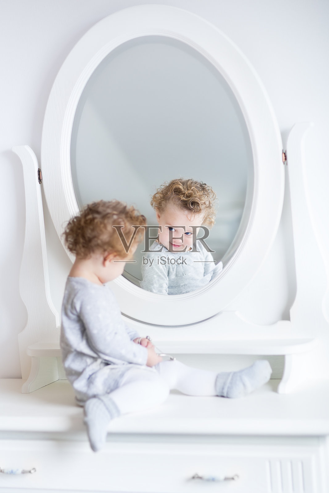 有趣可爱的小女孩看着她的反射与圆形的镜子照片摄影图片