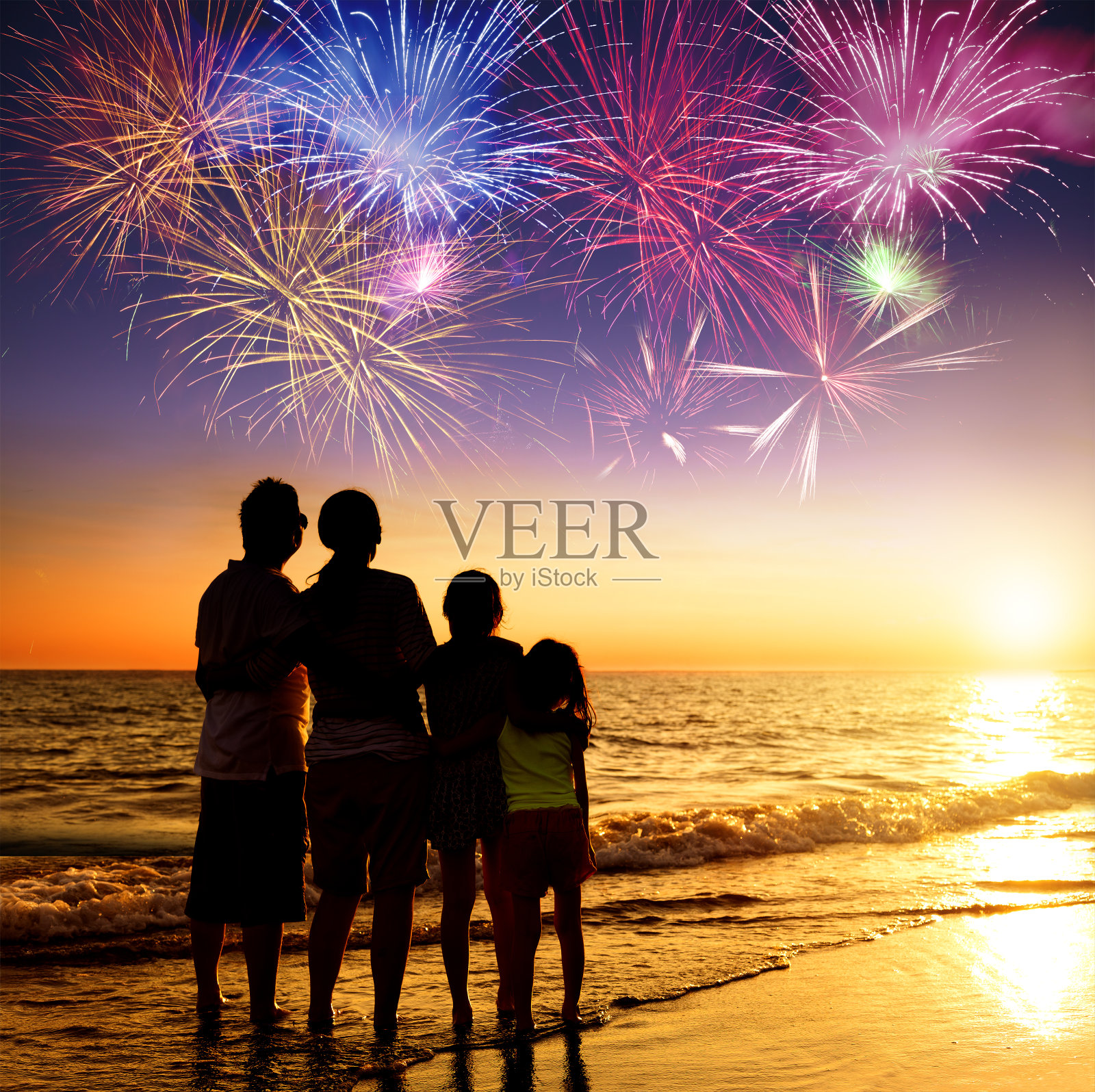 幸福的一家人在海滩上看日落和烟火照片摄影图片