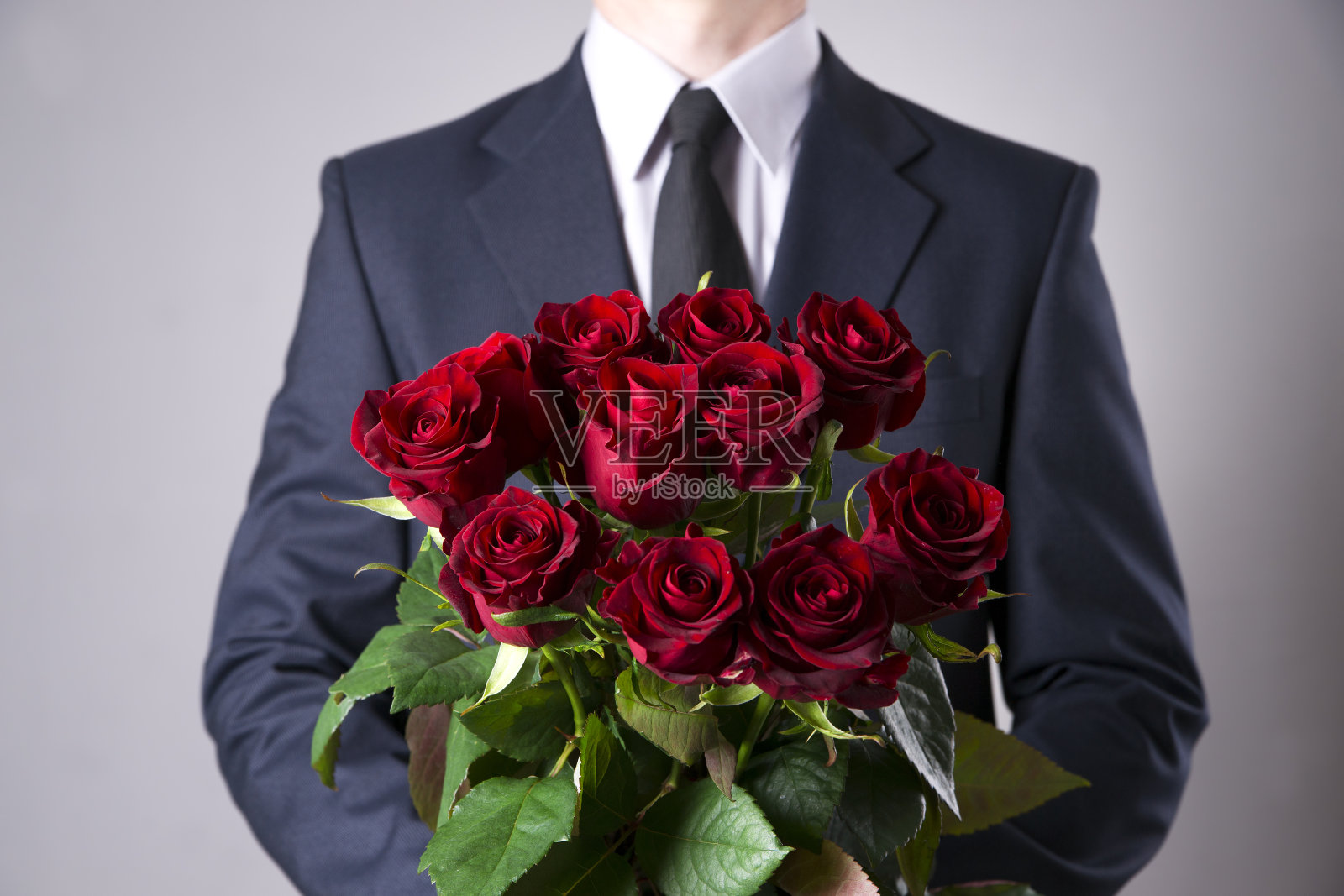 在灰色背景下，拿着一束红玫瑰的男人照片摄影图片