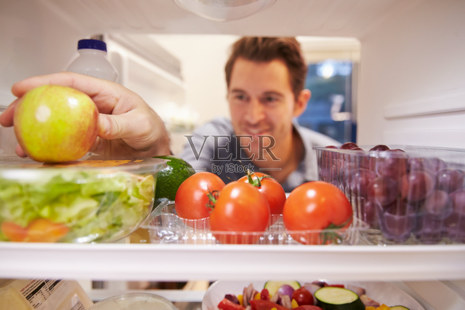 一名男子在看装满食物的冰箱并选择苹果照片摄影图片