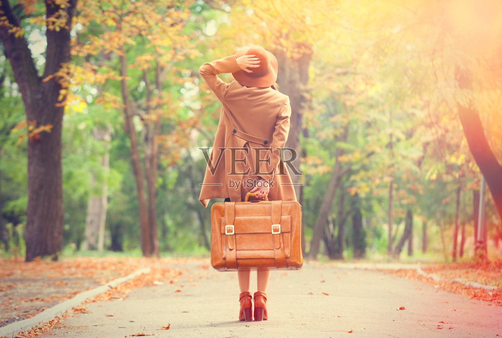 红发女孩提着手提箱在秋天的公园里。照片摄影图片