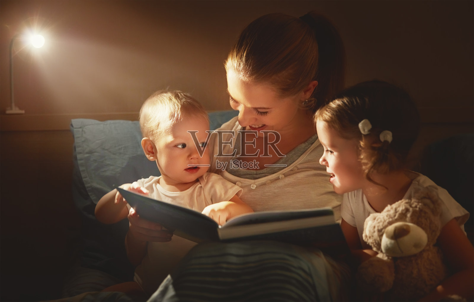 幸福的家庭妈妈和孩子们在床上看书照片摄影图片