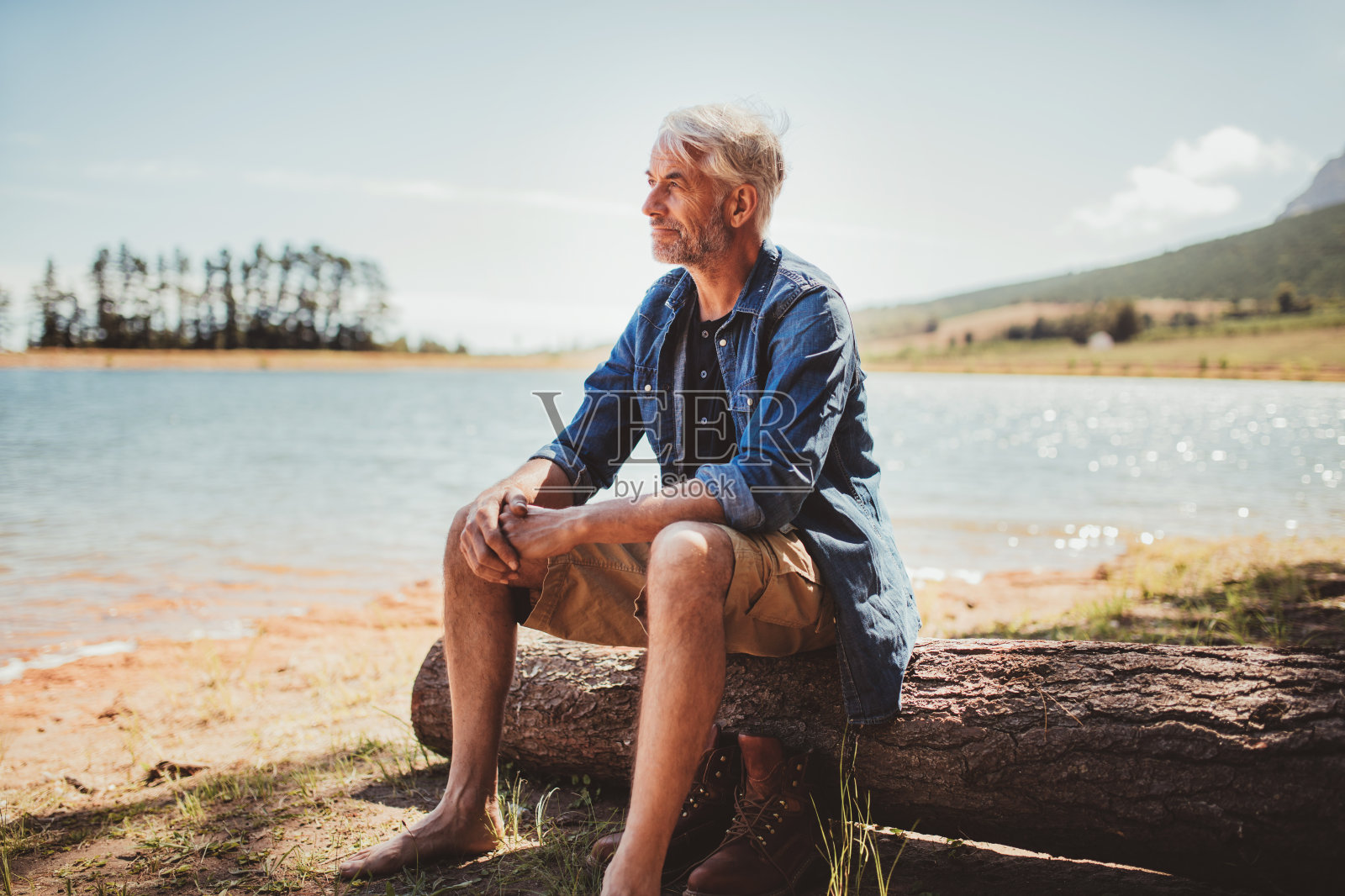 一个成熟的男人坐在湖边的原木上照片摄影图片