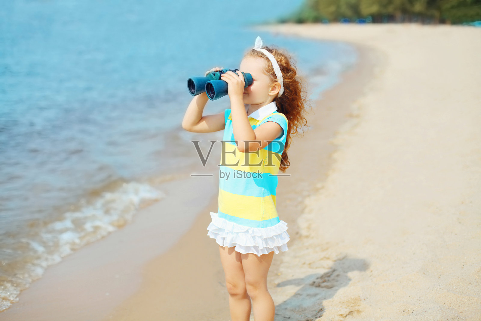一个小女孩在海边的海滩上用双筒望远镜看着照片摄影图片