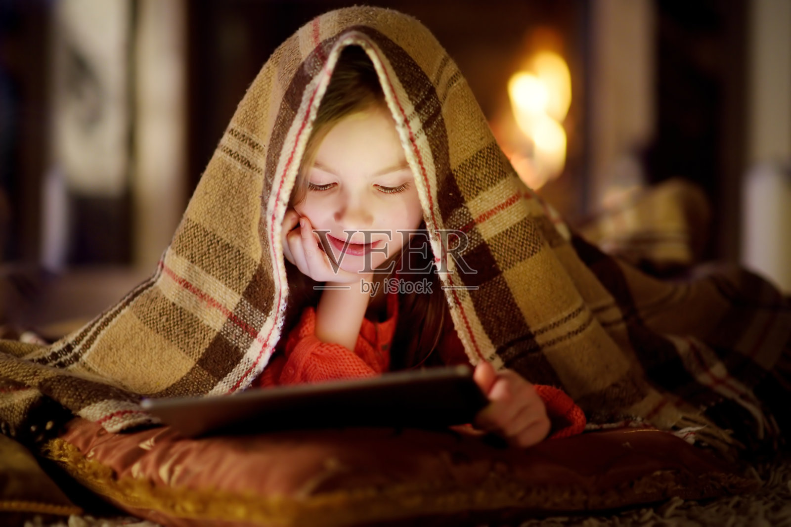 可爱的小女孩在圣诞节晚上壁炉旁使用平板电脑照片摄影图片