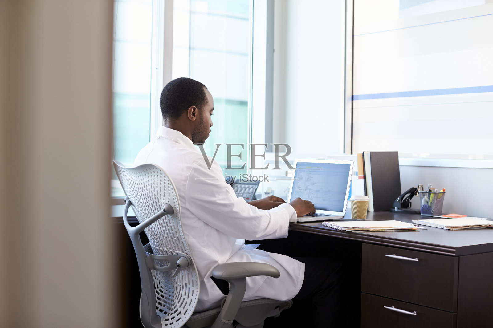 穿着白大褂在办公室用笔记本电脑工作的医生照片摄影图片