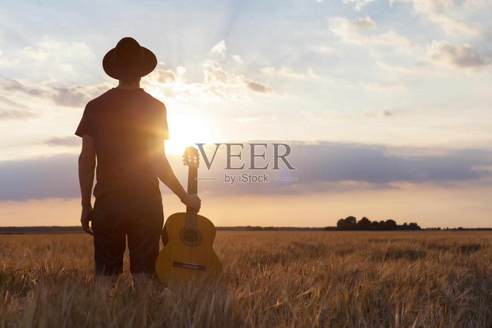 音乐家拿着原声吉他，走在夏日的田野里，夕阳西下照片摄影图片