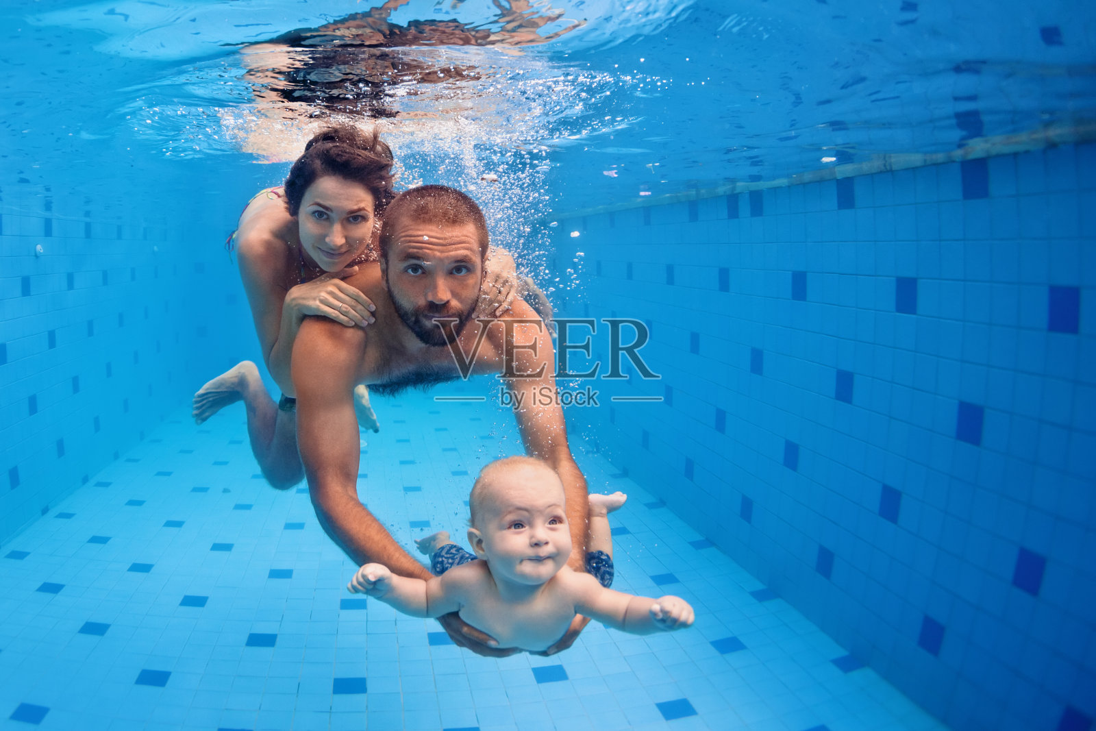 家庭在游泳池的乐趣。妈妈，爸爸，宝宝潜入水中照片摄影图片